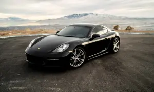 Czarny Porsche Cayman na tle gór i jeziora. Zastanawiasz się, ile kosztuje Porsche?