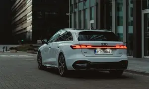 Białe Audi A5 Avant 2025 z nowoczesnym pasem świateł LED na klapie bagażnika, zaparkowane na tle szklanych budynków.