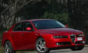 Czerwone Alfa Romeo 159 1.9 JTD z charakterystycznym grillem, zaparkowane na tle drzew.