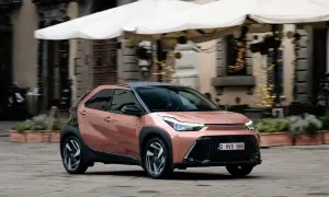 Różowy Toyota Aygo X z czarnym dachem jedzie po brukowanej ulicy.