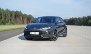 Szary MG3 Hybrid na betonowym placu, z lasem w tle.