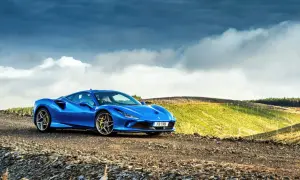 Niebieskie Ferrari F8 na tle malowniczego, pagórkowatego krajobrazu z chmurami na niebie.
