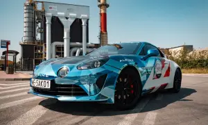 Błękitno-białe Alpine A110S z numerem 290 na tle przemysłowej zabudowy.