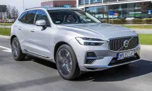 Srebrny Volvo XC60 T6 w ruchu miejskim, z kierowcą za kierownicą. Elegancki SUV na tle nowoczesnych budynków.