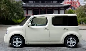 Biały Nissan Cube zaparkowany przed tradycyjną japońską świątynią.