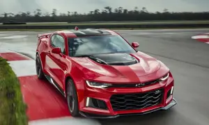 Czerwone Camaro ZL1 z czarnymi pasami pędzi po torze wyścigowym, zostawiając za sobą smugę prędkości.