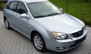Jasnosrebrny Kia Cerato hatchback stoi na chodniku z kostki brukowej.