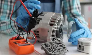 Mechanik w niebieskich rękawiczkach bada alternator samochodowy, sprawdzając, ile miedzi jest w alternatorze samochodowym. Obok leży multimetr i tłok.