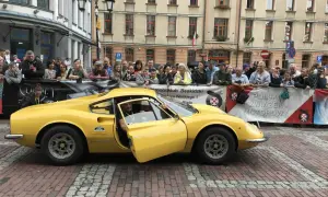 Żółte Ferrari Dino z otwartymi drzwiami, kierowca w środku, tłum widzów za barierką.