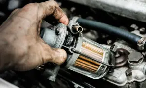 Brudna ręka mechanika wymienia jeden z filtrów w instalacji LPG. Widać przezroczysty korpus filtra z pomarańczowymi wkładami.