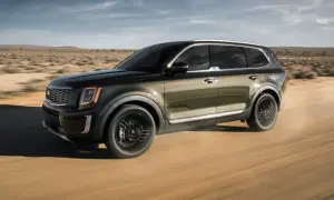 Ciemnozielony Kia Telluride przemierza pustynną drogę, unosząc kurz.