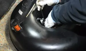 Ręce w rękawiczkach montują lub demontują okrągły zbiornik LPG w bagażniku samochodu.