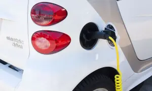 Biały samochód elektryczny z podłączonym żółtym kablem do ładowania.