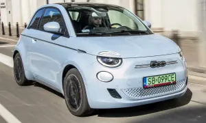 Jasnoniebieski fiat elektryczny 500e z czarnym dachem jedzie ulicą. Kierowca w okularach przeciwsłonecznych prowadzi auto.
