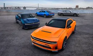 Pomarańczowy i niebieski Dodge Charger Hellcat obok szarego coupe, z mostem i miastem w tle.