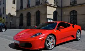 Czerwone Ferrari F430 zaparkowane na brukowanej ulicy przed kamienną budowlą.