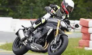 Motocyklista w kasku i kombinezonie pochyla się na torze wyścigowym na motocyklu Triumph Speed Triple.