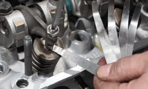 Mechanik sprawdza luzy zaworowe za pomocą szczelinomierza w silniku samochodowym.