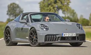 Szary Porsche Carrera Targa z otwartym dachem i kierowcą w okularach przeciwsłonecznych jedzie po drodze.