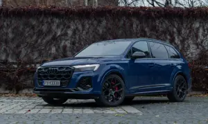 Elegancki, ciemnoniebieski Audi Q7 z czarnymi felgami i czerwonymi zaciskami hamulcowymi stoi na brukowanej nawierzchni.
