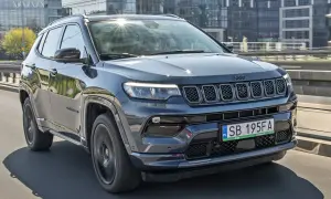 Ciemnoszary Jeep Compass 2025 na drodze, z nowoczesnymi budynkami w tle.