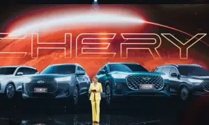 Kobieta w żółtym garniturze prezentuje nowe modele Chery Tiggo. Na ekranie za nią widnieje logo marki.