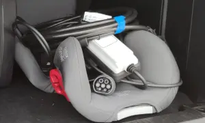 Kabel do ładowania samochodów elektrycznych leży na foteliku dziecięcym w bagażniku.