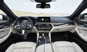 Wnętrze g30 bmw z jasną tapicerką, kierownicą i ekranem multimedialnym. Widok na pustynny krajobraz przez przednią szybę.