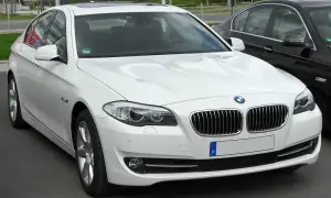 Białe BMW 535d z chromowanymi detalami i przyciemnianymi szybami, zaparkowane obok czarnego samochodu.
