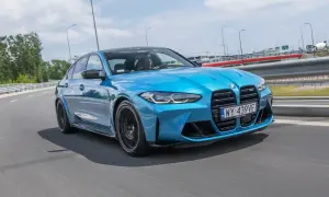 Niebieskie BMW M3 Competition pędzi po drodze, błyszcząc w słońcu.