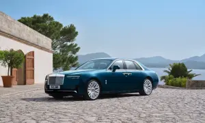 Elegancki Rolls-Royce Ghost w kolorze głębokiego turkusu zaparkowany na kamiennym dziedzińcu, z widokiem na morze i góry.