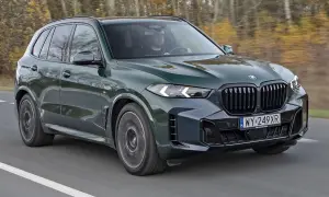 Zielony BMW X5 M50d pędzi po drodze, otoczony jesiennym lasem.