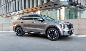 Elegancki, szary Kia Sorento 2025 z czarnymi felgami stoi przed nowoczesnym budynkiem.