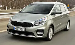 Srebrny Kia Carens 4 w ruchu drogowym, z widocznym grillem i reflektorami.