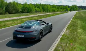 Szary Porsche Targa sunie po asfaltowej drodze, otoczony zielenią.