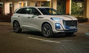 Biały Hongqi HS3 z charakterystycznym grillem i nowoczesnymi światłami stoi na mokrej, brukowanej ulicy nocą.