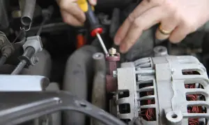Dłonie mechanika odkręcają śrubę przy alternatorze samochodu.