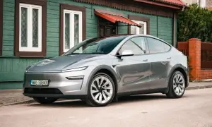 Srebrny Tesla Juniper, nowoczesny samochód elektryczny, zaparkowany przed tradycyjnym, zielonym domem z czerwonym dachem.