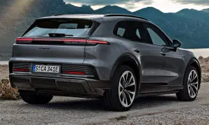 Nowe Porsche Cayenne w szarym kolorze, zaparkowane na kamienistej drodze z widokiem na góry i jezioro.