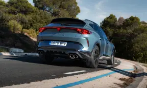 Tylna część Cupra Formentor VZ w kolorze szarym, z charakterystycznym pasem świateł LED, na krętej drodze wśród drzew.