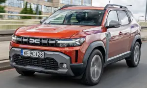 Pomarańczowy Renault Duster jedzie po drodze, z nowoczesnym designem i wyraźnym logo.