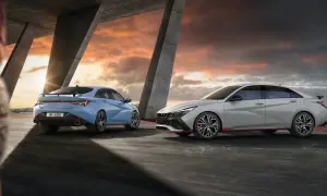 Dwa sportowe samochody Hyundai Elantra N, jeden niebieski, drugi jasnoszary, stoją pod betonowym mostem o zachodzie słońca.