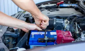 Ręce mechanika dokręcają klemę akumulatora. Widać silnik i elementy instalacji elektrycznej, czuć napięcie przed uruchomieniem.
