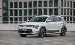 Biała Kia Niro na parkingu, z nowoczesnym budynkiem w tle. Sprawdź kia niro wymiary, by poznać jej kompaktową sylwetkę.