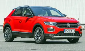 Czerwony, używany Volkswagen T-Roc z czarnym dachem i przyciemnianymi szybami, zaparkowany na tle białej ściany.