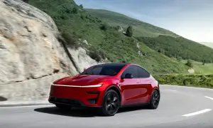 Czerwony Tesla Y Performance pokonuje zakręt na górskiej drodze, otoczony zielonymi wzgórzami i skalistymi zboczami.