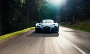 Niebieski Bugatti Mistral pędzi leśną drogą, słońce przebija się przez drzewa.