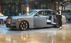 Elegancki szary Rolls-Royce Phantom z otwartymi drzwiami, obok stoi kobieta. Poznaj jego imponującą rolls royce cena.