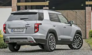Srebrny SsangYong Torres z polskimi tablicami rejestracyjnymi WN 7031S stoi na żwirowej drodze przed drewnianą bramą.