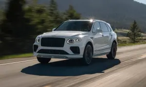 Biały Bentley SUV pędzi po krętej drodze wśród zielonych wzgórz.